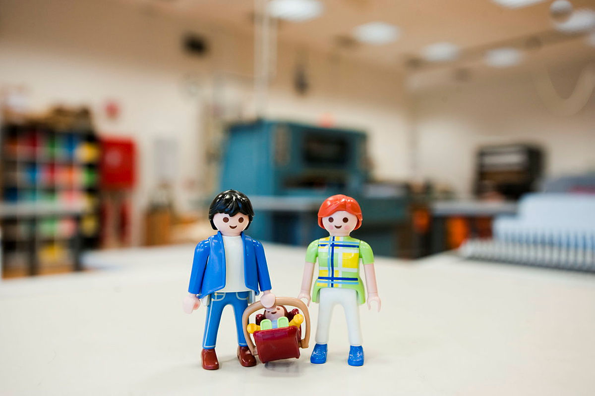 Playmobilfiguren stellen eine junge Familie mit Vater, Mutter und Baby in einer Bibliothek dar.